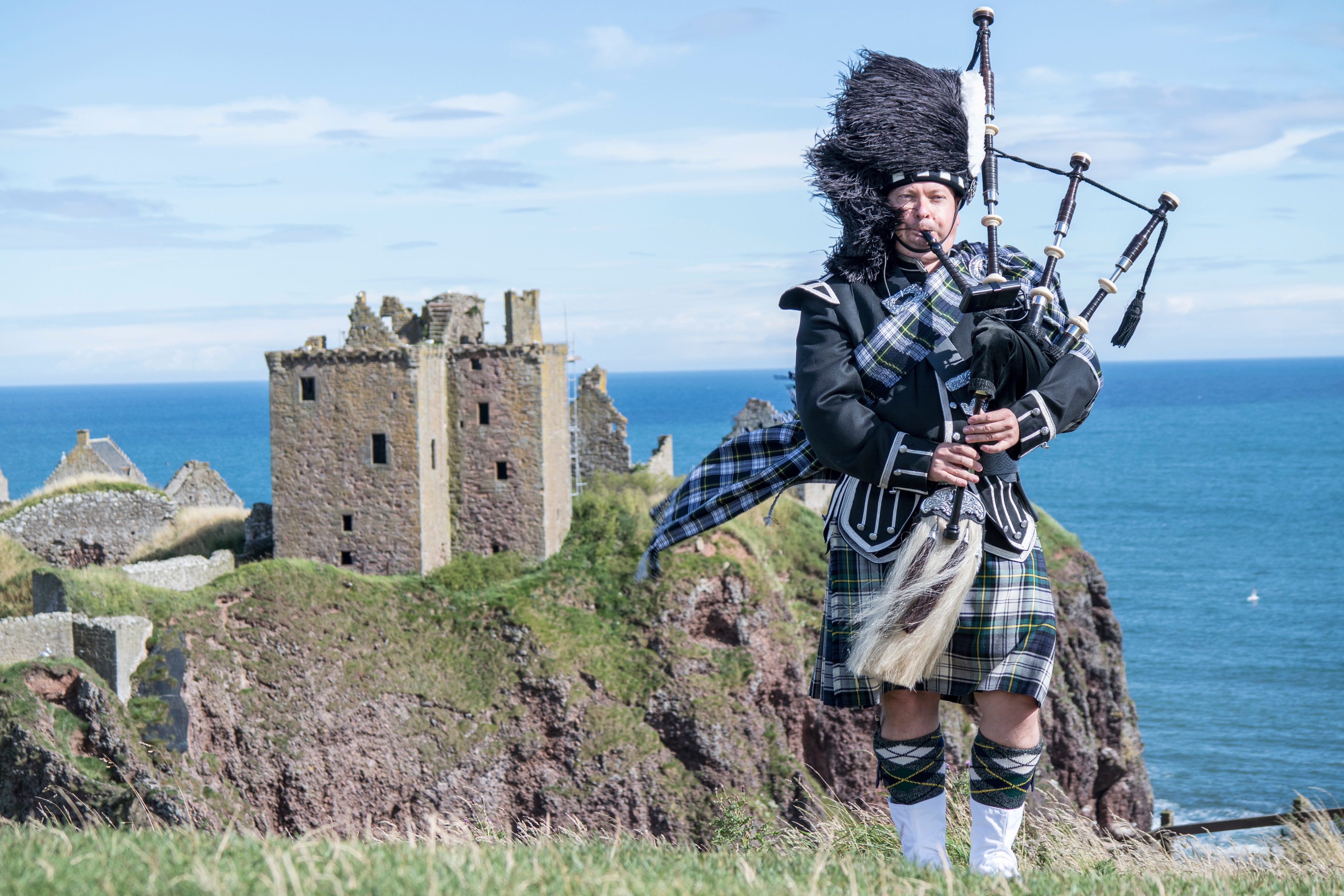 man playing bagpipes with castle in background