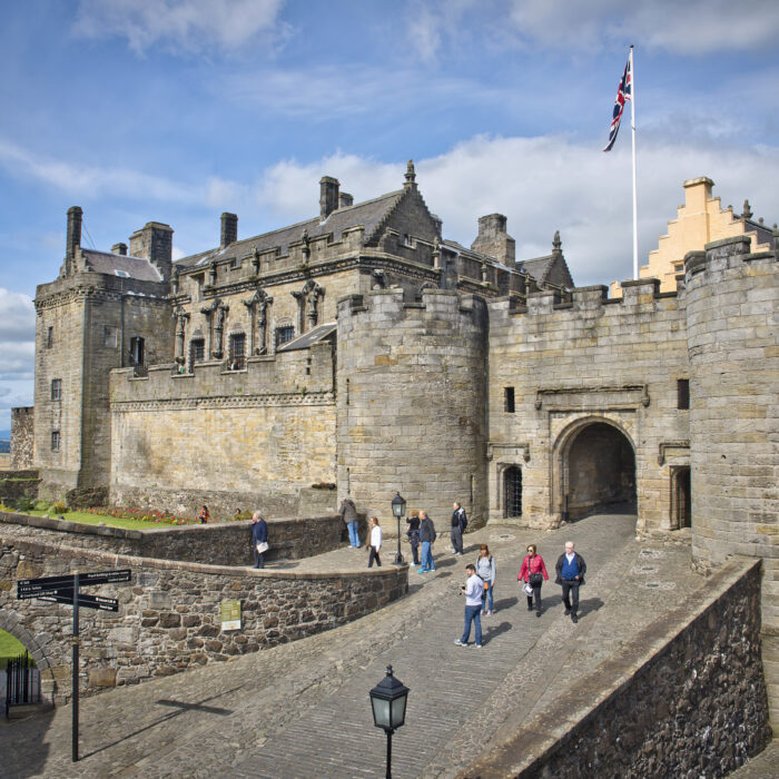 Stirling Castle, a historic royal palace in Scotland, perched atop a rocky outcrop, with its grand stone walls, towers, and battlements against a blue sky.